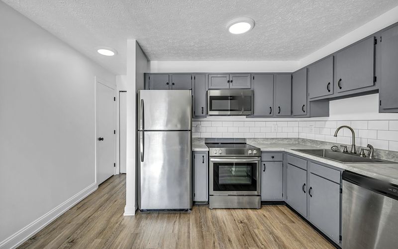 Apartment kitchen with gray cabinets, white subway tile, a stainless refrigerator, range, microwave and dishwasher