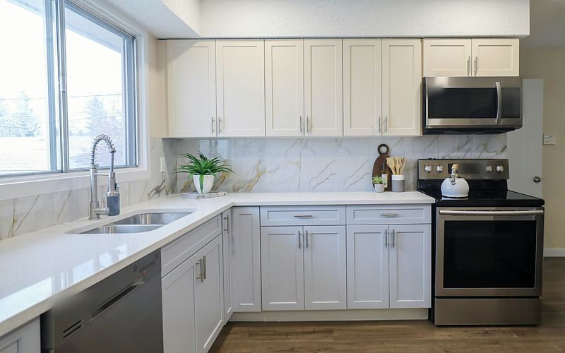 White kitchen with a sink under a wide window, a stainless electric range, over-the-range microwave and dishwasher
