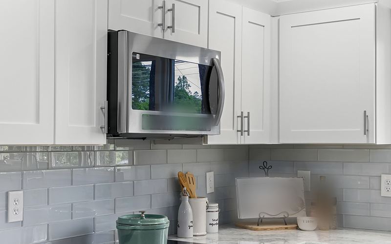 Stainless over-the-range microwave between white kitchen cabinets